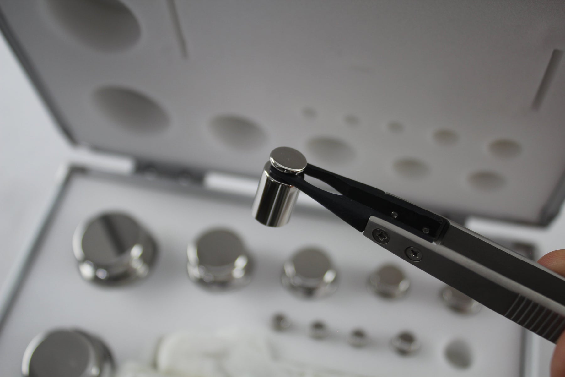 weighing scale calibration weight held by tweezers